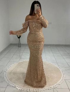 a woman is taking a selfie in a gold sequind gown with off the shoulder sleeves