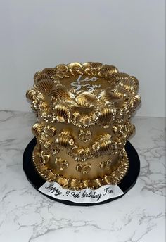 a three tiered gold cake on top of a black plate with the words happy birthday to you