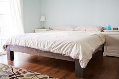 a bed sitting on top of a wooden floor next to a white dresser and window