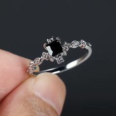 a hand holding a black diamond ring with white diamonds on the sides and an intricate band around it