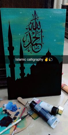 an islamic calligraphy book with paint and brushes on the table next to it,