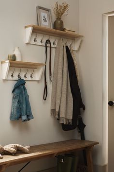 a wooden bench sitting under a coat rack next to a wall mounted shelf filled with coats