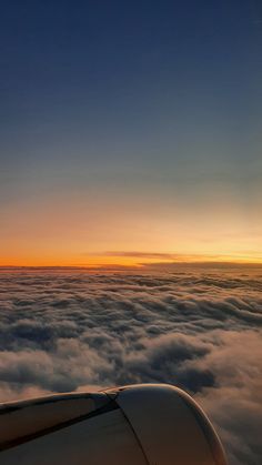 the wing of an airplane as it flies above the clouds at sunset or dawn in the sky