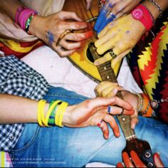 several people are sitting together with their hands on top of each other playing the guitar