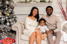 a man and woman sitting on a couch next to a baby in front of a christmas tree