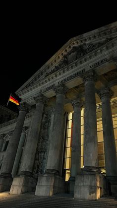 an old building with columns and flags on top at night, lit up by street lights