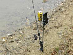 there is a fishing pole next to a yellow can on the ground by the water