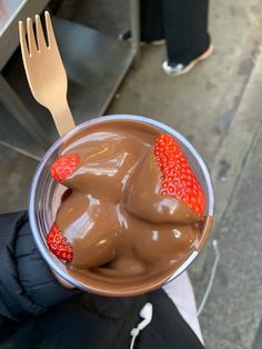 a person holding a cup with chocolate and strawberries in it