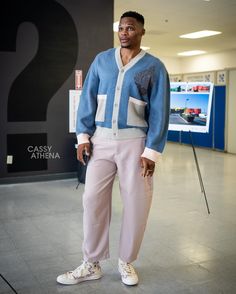 a man standing in front of a sign wearing pink pants and a blue cardigan sweater