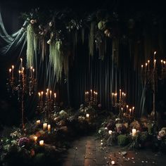 a dark room with candles and greenery on the wall, surrounded by flowers and moss