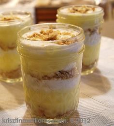 three desserts in small glass jars sitting on a table with other food items around them