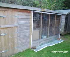 a chicken coop in the grass next to a wooden shed with a run down roof