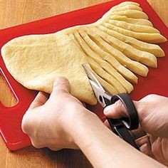 a person cutting up food on a red cutting board with a pair of scissor