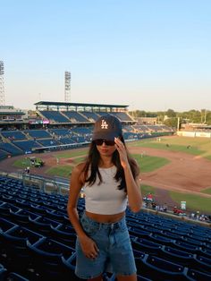 a woman standing in the stands at a baseball game wearing a hat and denim shorts