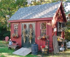 a red shed sitting in the grass next to a wooden table and bench with flowers on it