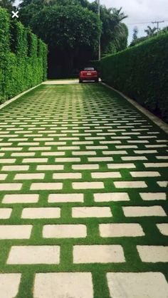 a red car driving down a street next to lush green hedges