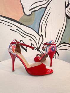 a pair of red high heeled shoes sitting on top of a white table next to a painting