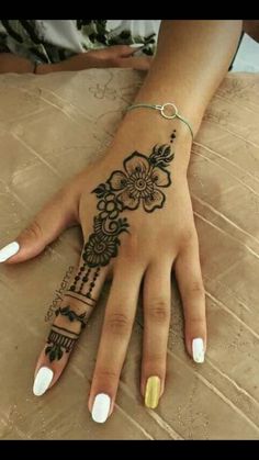 a woman's hand with a henna tattoo on her left wrist and white nails