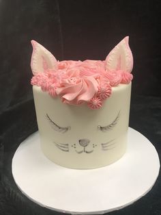 a white cake with pink frosting and cat's face on top, sitting on a plate