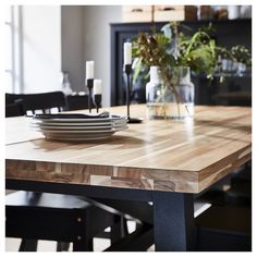 a wooden table with plates on it in a room filled with black chairs and plants