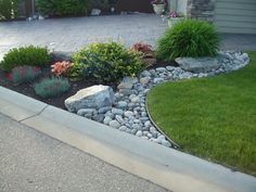 a rock garden in front of a house with grass and flowers on the side walk