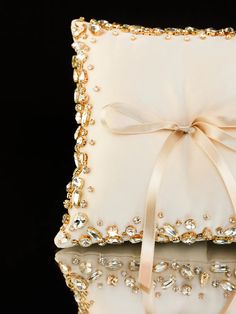 a white pillow with a bow on the side and pearls in the middle, sitting next to a black background