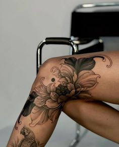 a woman sitting in a chair with her legs crossed and flowers on the leg tattoo