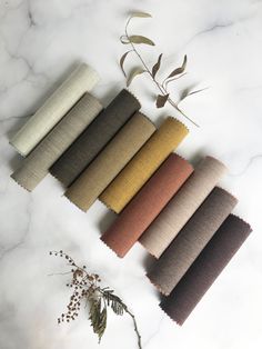 five different colors of fabric laid out on a white marble surface with dried plants in the background