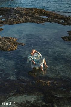 a woman is sitting on the rocks in the water