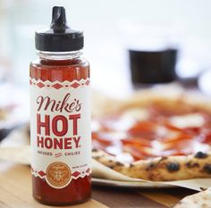 a bottle of mike's hot honey sits on a table next to a pizza