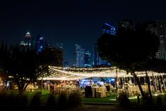 an outdoor event with lots of lights on the trees and buildings in the background at night