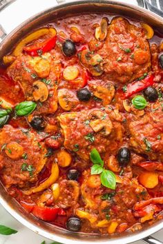 a pan filled with meat and vegetables covered in marinara sauce, garnished with fresh basil leaves