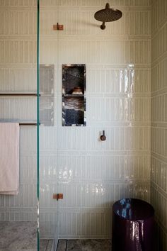 a bathroom with a glass shower door and white tiled walls next to a purple stool