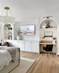 a bedroom with white walls and wood flooring has a bed, desk, chair, bookshelf and artwork on the wall