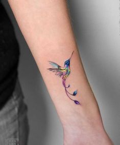 a small hummingbird tattoo on the wrist is shown in blue and pink colors, with an orange tail