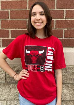 a woman standing in front of a brick wall wearing a chicago bulls t - shirt