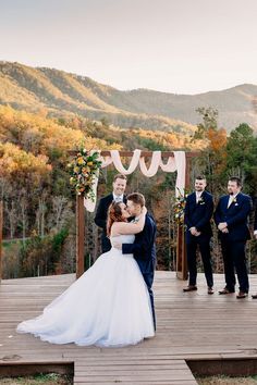 the bride and groom are hugging at their outdoor wedding ceremony in front of an autumn mountain backdrop