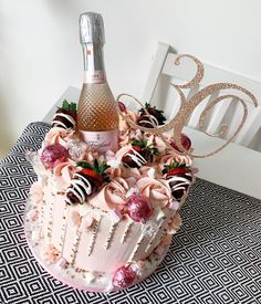 a pink cake with strawberries and chocolates on it, next to a bottle of champagne