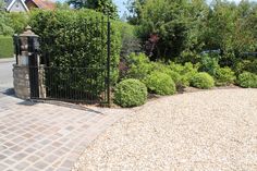 an iron gate is surrounded by gravel and shrubbery in front of a brick driveway