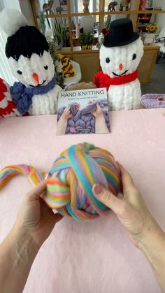 someone is holding a ball of yarn in front of two stuffed snowmen on the table