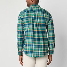 a man wearing a green and blue plaid shirt with white pants standing in front of a wall