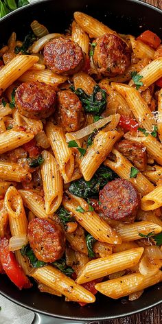 pasta with sausage, spinach and tomatoes in a skillet on a wooden table