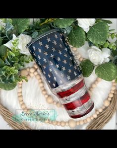 the american flag tumbler is sitting on top of some flowers and greenery with beads around it