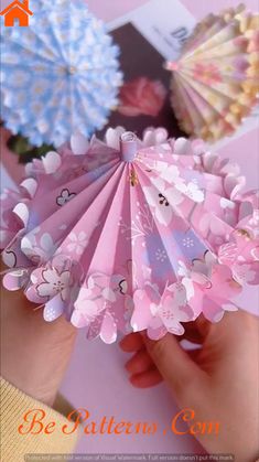 a person holding several paper fans in their hands on a pink table with flowers and pictures behind them