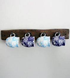 four cups are hanging from a wooden rack on the wall, which is decorated with blue and white designs