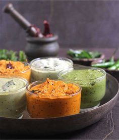 four small bowls filled with different types of dips on a plate next to vegetables