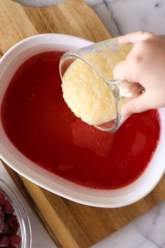 someone pouring red liquid into a white bowl with raspberries in the background on a wooden cutting board