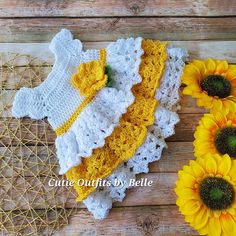 crocheted baby clothes and sunflowers on wooden background