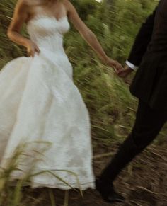 a bride and groom holding hands walking through the grass in front of some tall grasses