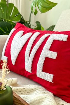 a red and white pillow sitting on top of a couch next to a potted plant